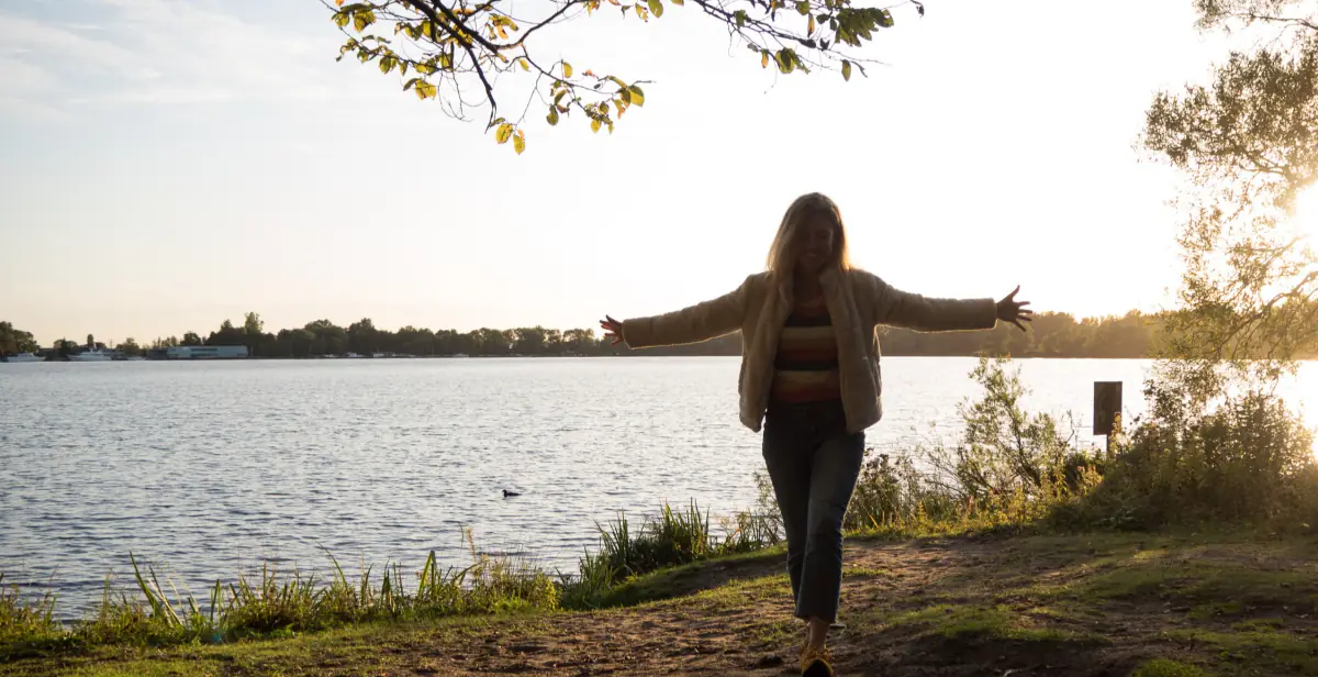 Anneke loopt met gespreide armen langs het water bij zonsondergang